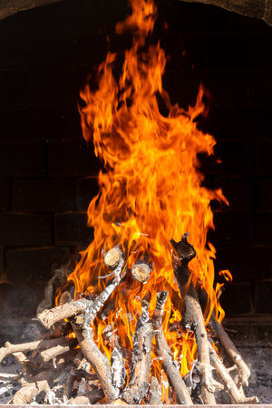A high bonfire with sharp tongues of bright yellow and orange flames on a dark smoke background in...