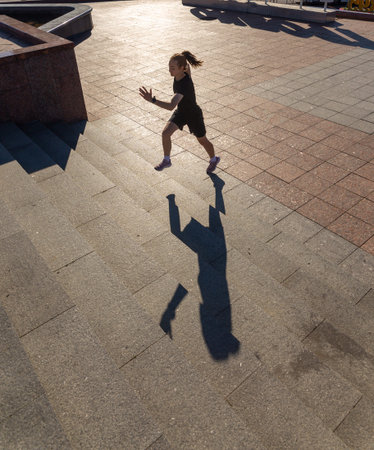 A young woman in black clothes running on stairs at city street early morning.の写真素材