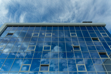 Architectural detail of the facade with multiple reflections of cloudy sky and the sun. Exterior of modern building. Architecture abstract backgroundの写真素材
