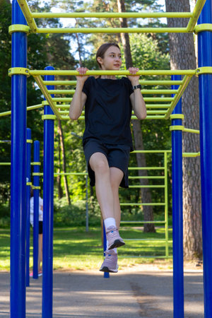 Portrait of beautiful teen age athletic girl training outdoors at open air gym at summer sunny day,...