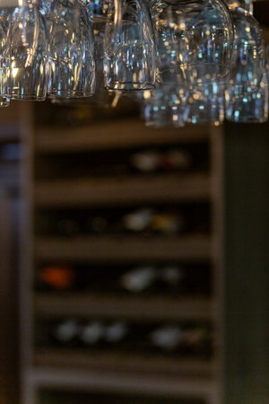 Clean wine glasses hanging over the bar counter on out of focus background with shelf with bottles...