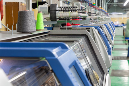 A row of industrial textil flat knitting machines in a knitwear factory. An industrial line of modern automatic knitting machines arranged in a row.の写真素材
