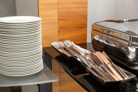 Stack of plates next to closed chafing dishes at party banquet hall. Marmites ready for service made...