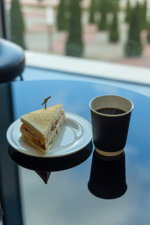 Paper cup of coffee and sandwich in the garden on a glass table with a reflection of the sky. Vertical image.の写真素材