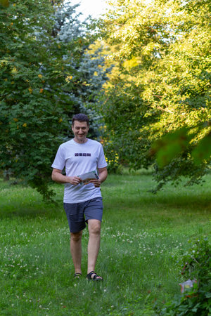 Grodno, Belarus - 26 June, 2024: Strong caucasian young man wearing sportswear running through a park during exercise in outdoor orienteering Street-O. Hobby sport.のeditorial素材