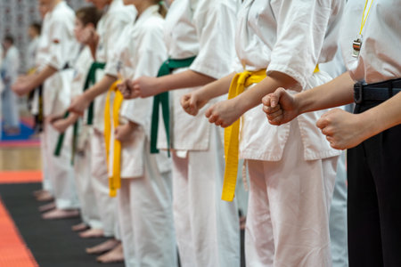 A close-up of a row of young athletes in white karate kimonos with clenched fists. A photo for a demonstration or karate competition. Energy and concentration concept.の写真素材