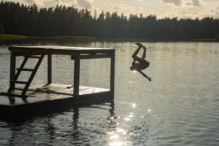 Teenage boy jumping in lake water at summer holiday. The concept of a happy carefree childhood.の写真素材