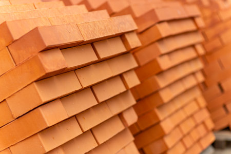 Stacks of new, red ceramic brick stacked on wooden pallets. Lots of new orange build bricks wall background and texture. Real estate construction, renovations. Selective focus.の写真素材