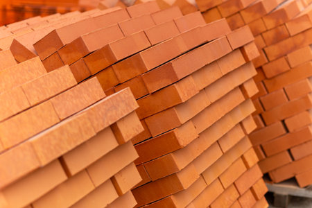 Stacks of new, red ceramic brick stacked on wooden pallets. Lots of new orange bricks wall background and texture. Real estate construction, renovations. Selective focus.の写真素材