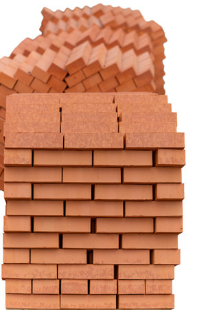 Stacks of new, red ceramic brick stacked on wooden pallets. Lots of new orange build bricks wall background and texture. Selective focus. Isolated on white.の写真素材