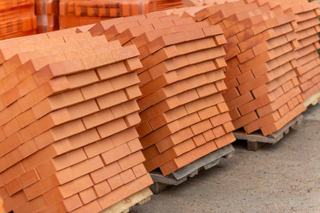 Stacks of new, red ceramic brick stacked on wooden pallets. Lots of new orange build bricks wall...