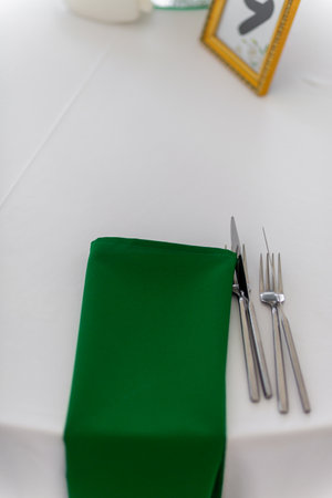 Close up of wine glasses, silver tableware and green napkins on round tables covered with white tablecloth. Catering concept. Interior of tent for wedding dinner, ready for guests.の写真素材