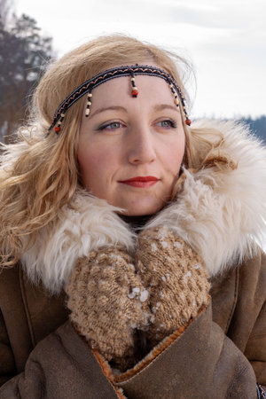 A young woman with blonde hair dressed in a warm fur-lined leather coat with boho-style accessories, on the riverbank on a snowy winter dayの写真素材