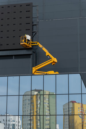 Two workers in hard hats mount elements of outdoor video advertising on a gray wall of a building against a sky with cloudsの写真素材