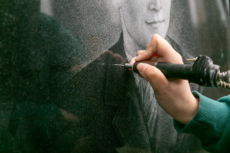 The hand of a female artist who applies images to monuments by hand engraving. A workshop for the manual manufacture of monuments.の写真素材