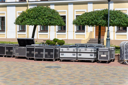 Stacked boxes near a stage under neatly trimmed trees, ready for an outdoor event or performance.