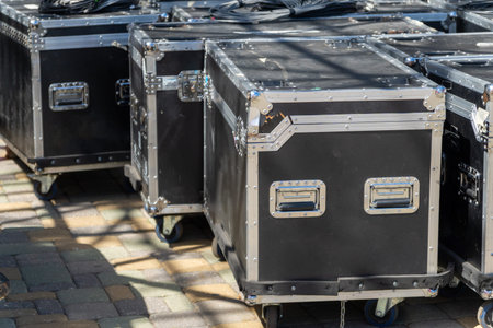 Boxes with sound and lighting equipment and cables near a concert stage during setup. Preparing for an outdoor music show with professional audio gear.の写真素材