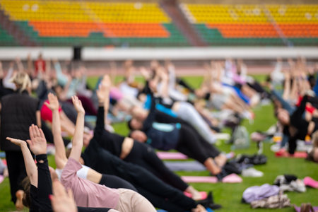 A blurred, indistinct crowd of people participating in a large group activity or exercise class at a stadium on a sunny summer day.の写真素材