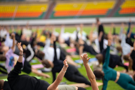 Group yoga session on stadium lawn, shallow depth of field focusing on one practitioner. Connection, wellness, fitness community.の写真素材