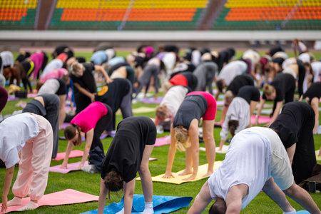 Group yoga session on stadium lawn in FYSM style, shallow depth of field focusing on one practitioner. Connection, wellness, fitness community.の写真素材