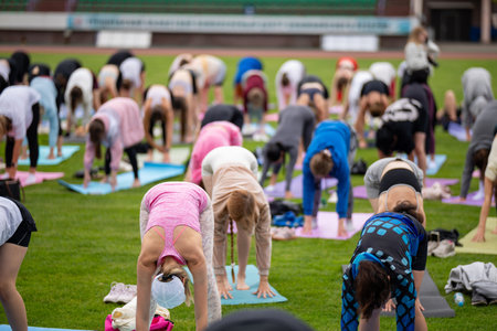 Group yoga session on stadium lawn in style, shallow depth of field focusing on one practitioner. Connection, wellness, fitness community.の写真素材