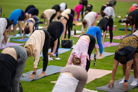 Group yoga session on stadium lawn, shallow depth of field focusing on one practitioner. Connection, wellness, fitness community.の写真素材