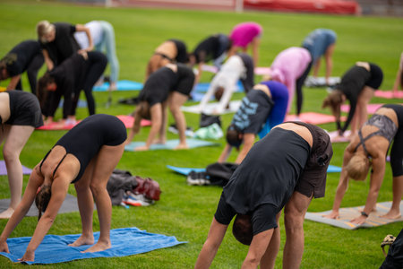 Group yoga session on stadium lawn in FYSM style, shallow depth of field focusing on one practitioner. Connection, wellness, fitness community.の写真素材