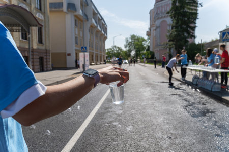 A close-up of a volunteer's hand offering a cup of water to a marathon runner on a city street during a race.の写真素材