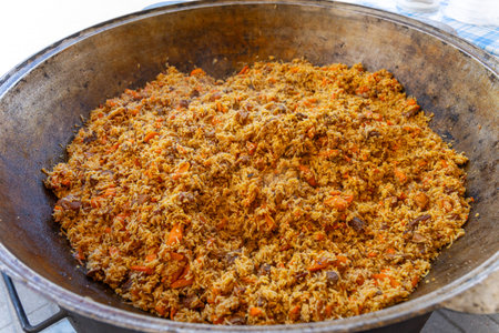 A large metal cauldron with freshly prepared Uzbek pilaf steams at a vibrant street food festival,...