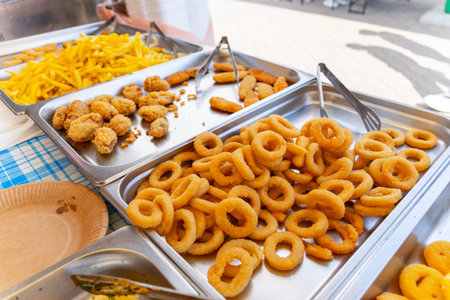 Trays of crispy fried onion rings, chicken nuggets, and French fries ready for serving at a...