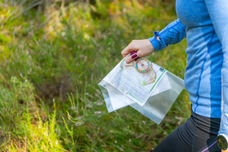 Orienteering athlete running through a summer forest with a map and compass. Close-up, selective focus on the map in his hands.の写真素材