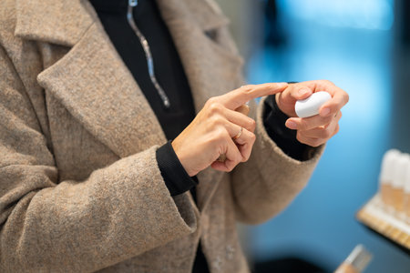 A close-up of a woman's hands, one holding a white cosmetic product and the other using a finger to test it. The photo emphasizes skincare, beauty, and product testing.の写真素材