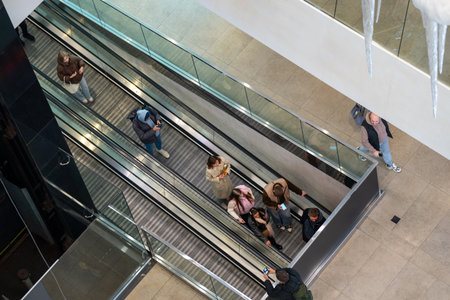 High-angle shot of people on escalators inside a modern shopping mall. The scene captures the dynamic urban lifestyle and consumer activity with contemporary architecture.の写真素材
