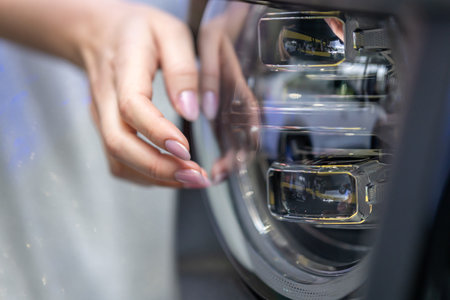 A close-up shot of a woman's hand touching a modern car headlight with a futuristic, multi-cube design, highlighting the vehicle's technology, style, and innovation.の写真素材
