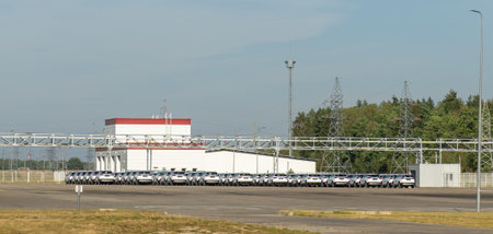 A vast outdoor storage lot at an automotive factory is filled with rows of brand-new, white cars...