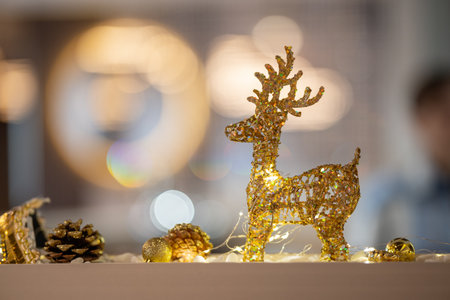 A decorative golden glitter reindeer figurine is the focal point of a festive indoor Christmas display, featuring bokeh lights, pine cones, and a cozy holiday ambiance.の写真素材