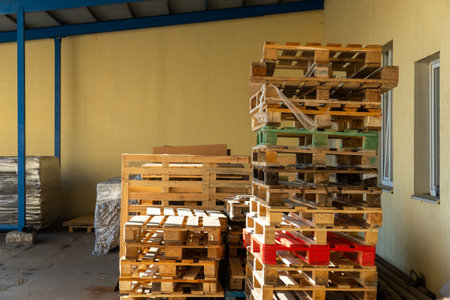 Stacks of wooden pallets are stored in an industrial warehouse yard, ready for shipping, transport,...