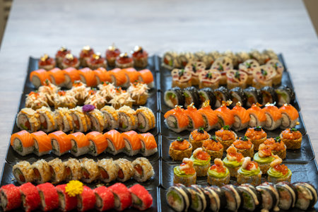 A vibrant array of many different types of gourmet sushi and maki rolls, showcasing diverse flavors and artistic presentation, is arranged on black plates for catering.の写真素材