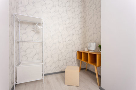 Minimal dressing room interior with open clothing rack, hangers, wooden vanity table with mirror, and stool. Clean bright space with patterned wallpaper, ideal for wardrobe and storage.の写真素材