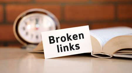 Broken links concept text on a white background with a clock and an open bookの写真素材