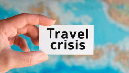 Travel crisis - text on a white sheet in hand against the background of the atlas mapの写真素材