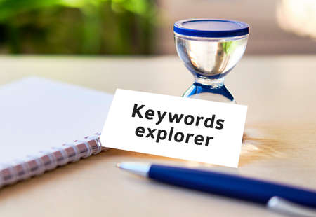 Keyword rank - business seo concept text on a white notebook and hourglass clock, blue pen, green leaves of flowersの写真素材