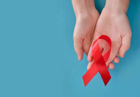 Red symbolic ribbon - the problem of AIDS, vasculitis, anorexia, drug abuse. Two crossed hands on a blue backgroundの写真素材