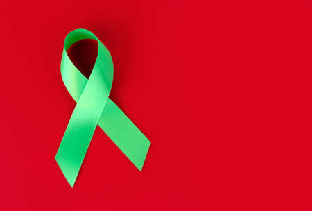 Green symbolic ribbon - the problem of organ donation, mental health. On a red backgroundの写真素材