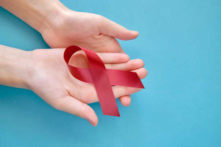 Dark red symbolic ribbon - the problem of disabled people and amyloidosis. Two crossed hands on a blue backgroundの写真素材