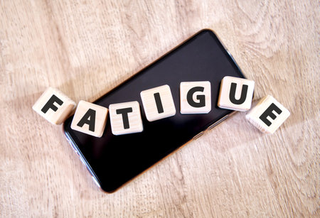 Text fatigue on wooden cubes on a black smartphone. Cubes lay on a black smartphone on the wooden table.の写真素材