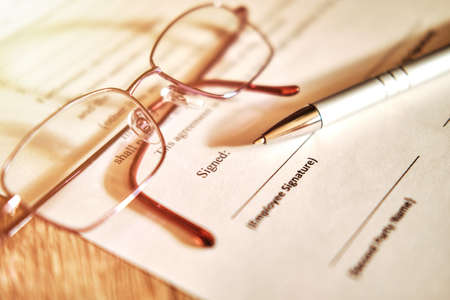 Contract sheet with glasses and a pen on a wooden backgroundの写真素材