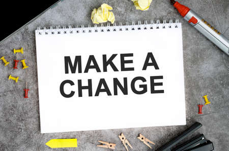 Make a change text on a white notebook with pins, marker and stapler on a concrete tableの写真素材