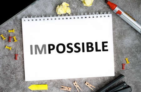Impossible text on a white notebook with pins, marker and stapler on a concrete tableの写真素材