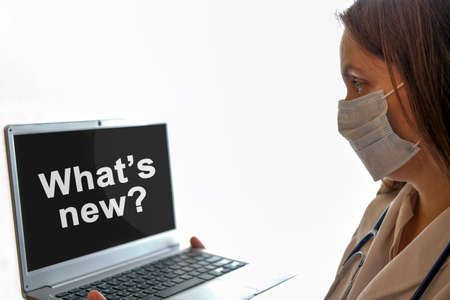 Doctor woman in a mask with stethoscope looks at the monitor screen where the text Whats new is writtenの写真素材